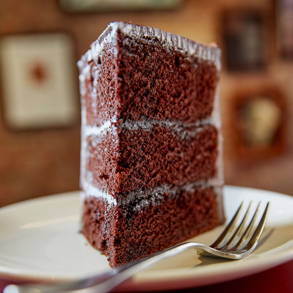 Close up looking into the point of a slice of chocolate layer cake - on a plate with a fork, blurred background