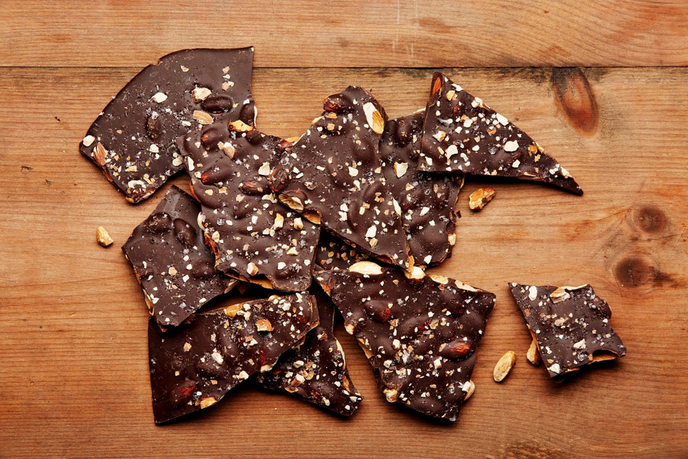 
                  
                    Large pieces of dark chocolate bark with almonds and sea salt on a rustic wooden tabletop
                  
                