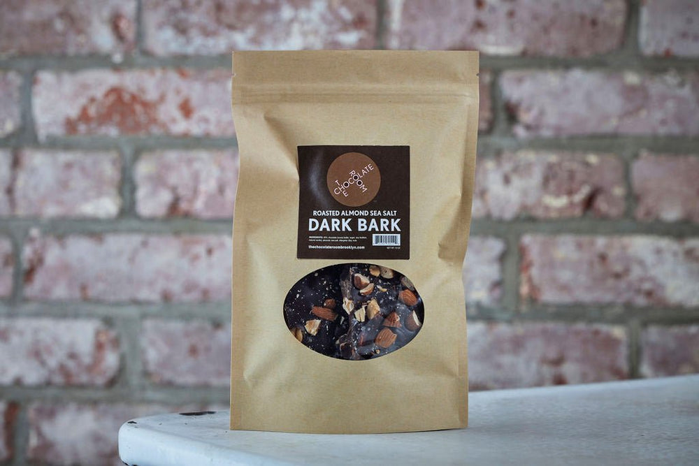 Craft pouch of dark chocolate bark, with visible chunks of almonds, sea salt and chocolate through a clear window on front