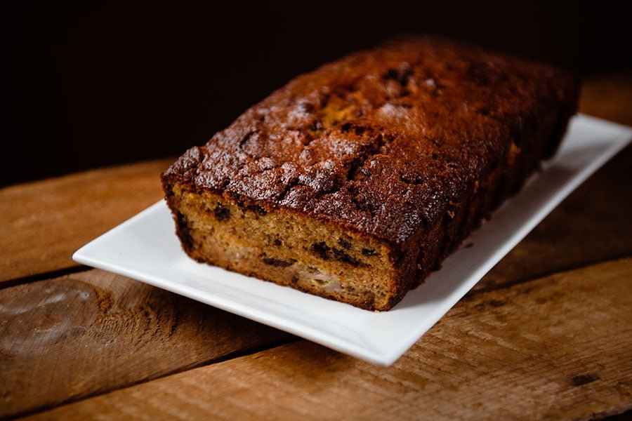 Fresh baked chocolate banana bread with first piece cut off on a white plate on a recycled create tabletop - moody