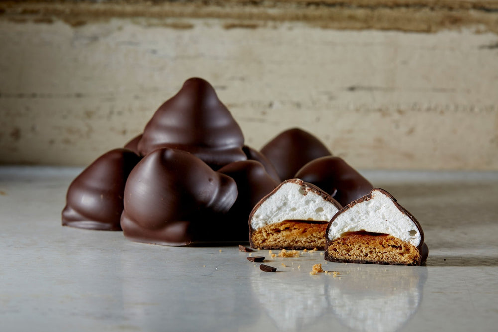 A stack of dark chocolate s'mores with 1 cut in half revealing the graham cracker and domed marshmallow, with crumbs.