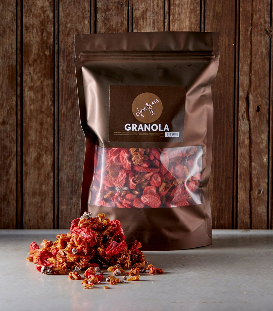 
                  
                    Resealable bag of granola in front a rustic wooden panel with pile of granola showing chunks of chocolate and strawberries
                  
                