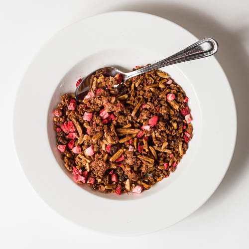 
                  
                    Overhead view of a white bowl filled with granola. The bowl has a spoon in it
                  
                