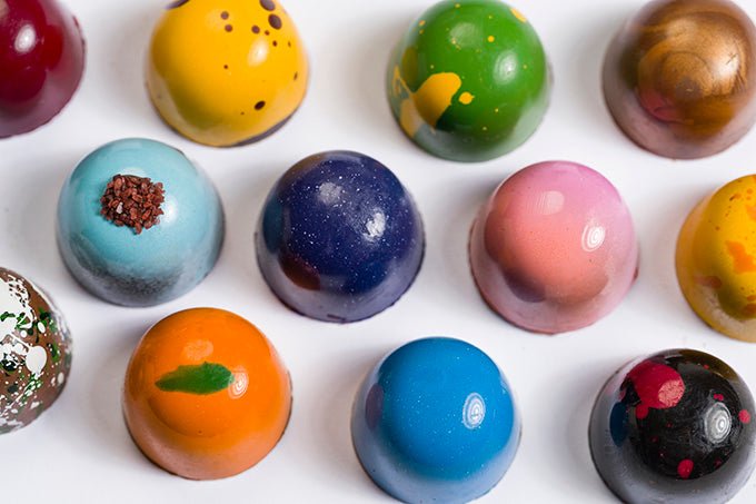 
                  
                    Overhead, close up view of 12 assorted colorful hand painted bonbons
                  
                