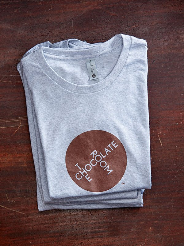 A stack of The Chocolate Room branded t-shirts, grey t-shirt, brown logo on a recycled wooden tabletop